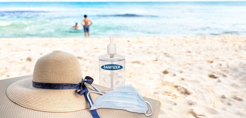 gel hydroalcoolique, masque, chapeau et lunettes de soleil installée sur la plage