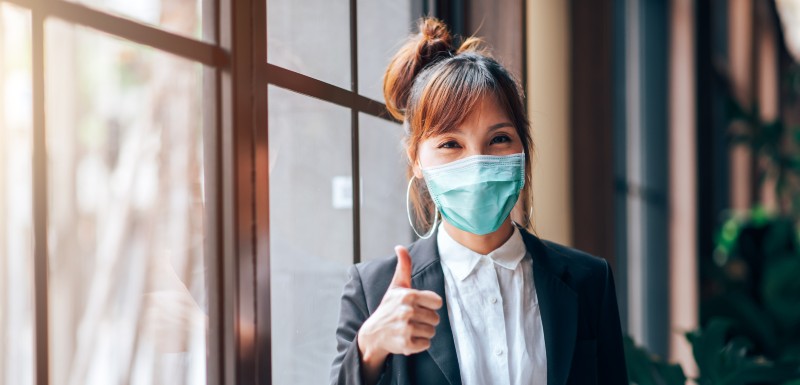 Jeune femme qui porte un masque faisant signe que tout va bien avec le pouce en l'air